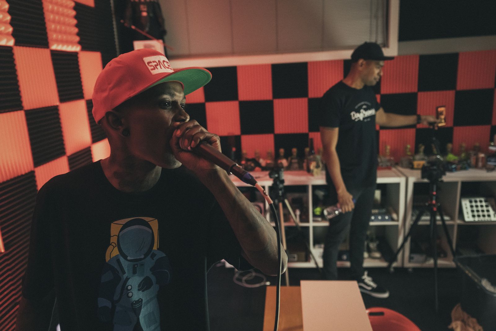 An MC on the mic during a studio session, someone working the desk behind